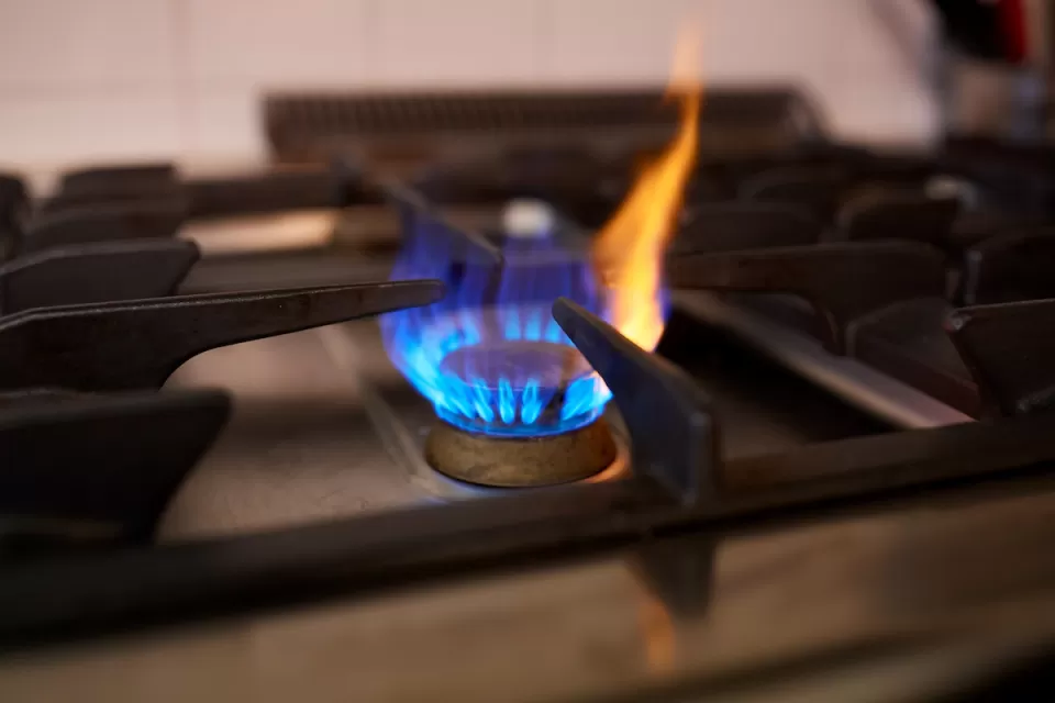 Close-up of lit burner on natural gas stove with blue flame and small yellow flame shooting up.